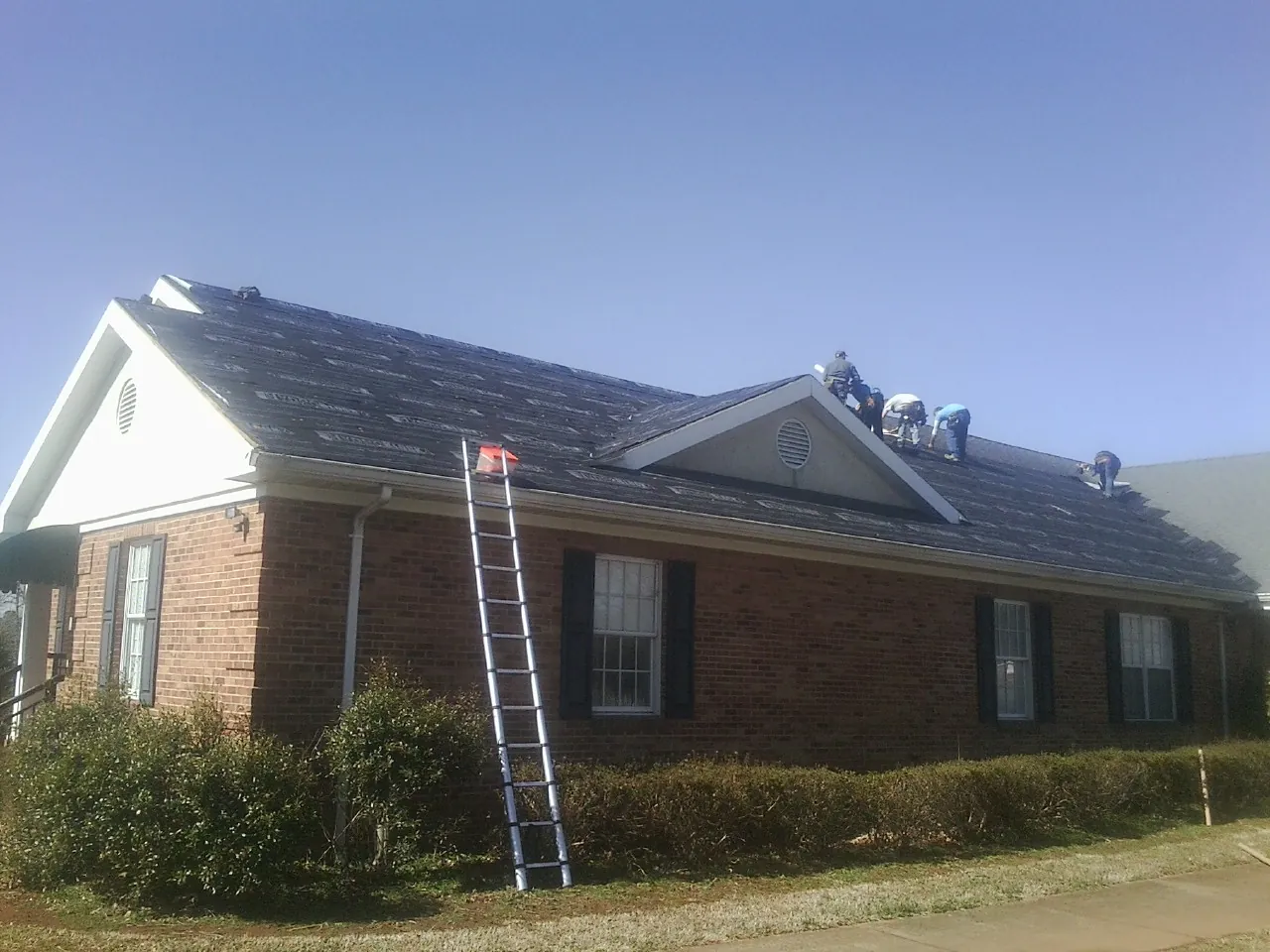 Crew tearing shingles off a brick ranch roof with a ladder set — Emergency Roof Repair work by our crew in Folly Beach