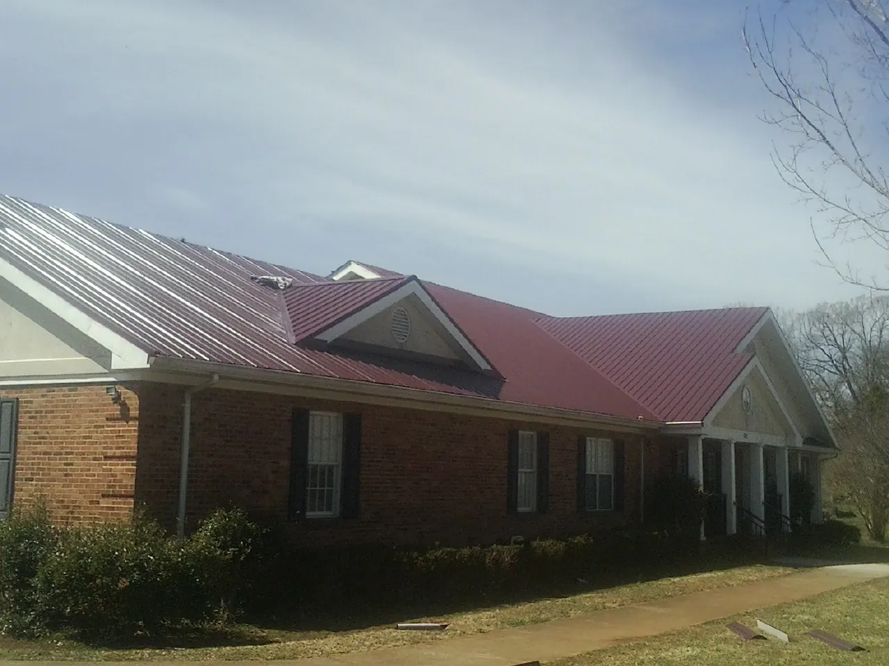 Red metal roof with gabled entries on a long brick building, from a Hail Damage Roof Repair job in Folly Beach