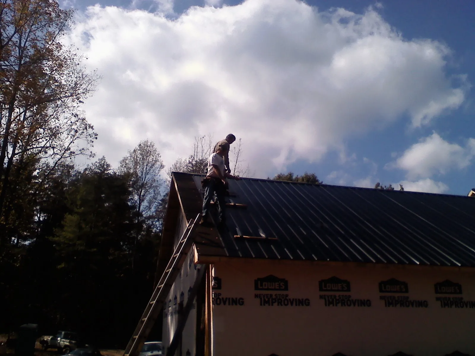 Roofer fastening dark metal panels high against a cloudy sky, from a Roof Inspection job in Folly Beach